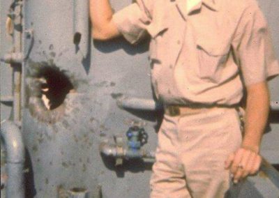 USS Liberty officer poses in front of damage to ship